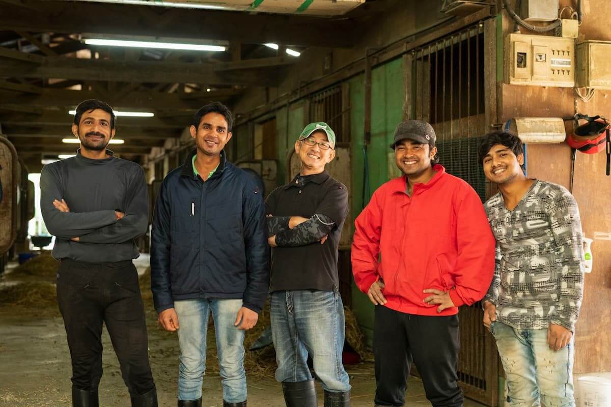 作業場で笑顔で並んでいる5人の男性